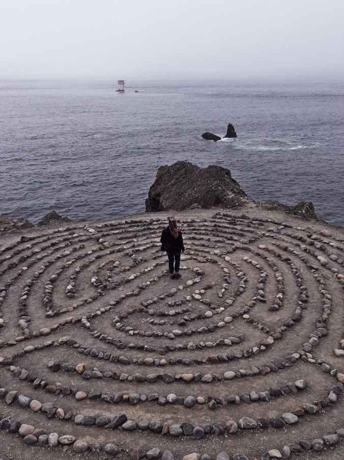 unrecognizable woman in center of stony labyrinth on seashore